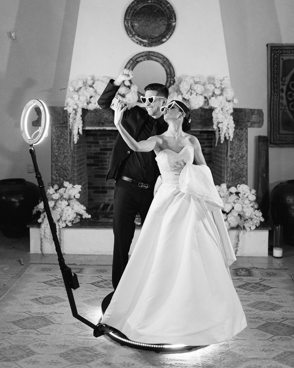 Novios con gafas de corazón bailando sobre la plataforma 360º, en blanco y negro